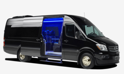 A black Mercedes-Benz van with an open door, revealing a blue-lit interior and spacious seating.